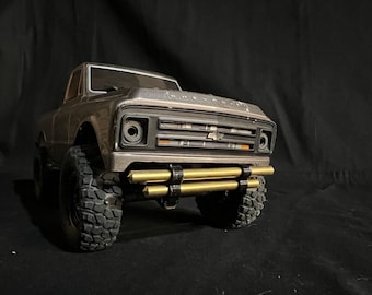 Puede incluir: Modelo detallado, marrón, de una camioneta Chevrolet. El camión presenta una parrilla negra, neumáticos grandes y un parachoques dorado. La palabra "CHEVROLET" es visible en el capó. El camión está sobre un fondo oscuro.