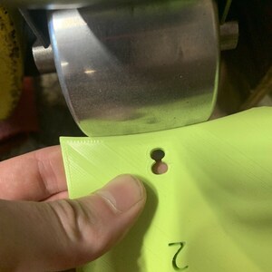 May include: A lime green 3D printed plastic part with a hole and the number "2" printed on it.