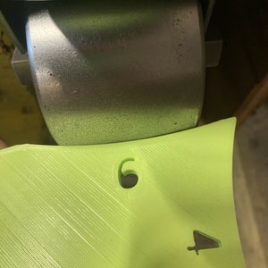 May include: A lime green plastic part with a number "6" and a small arrow symbol. The part is attached to a metal wheel.