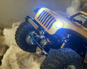 May include: A yellow toy Jeep with black wheels and a black bumper. The Jeep has headlights and a windshield. The Jeep is on a rocky surface.
