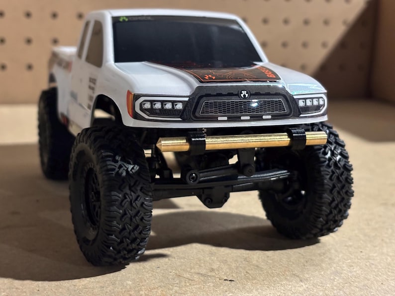 May include: A white and black toy truck with large black tires. The truck has a gold-colored bumper and a black grill. The front of the truck has a series of lights. The truck is a miniature replica.