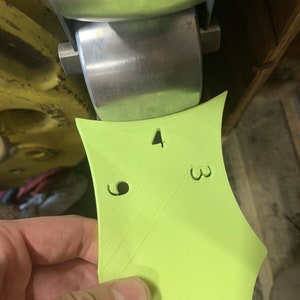 May include: A lime green plastic template with numbers 2, 3, and 4 printed on it. There are two holes in the template.