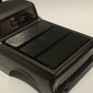 May include: A gray pickup truck with a black bed cover. The bed cover has three sections that fold up. The truck has a "Muc-Off+" sticker on the back window.