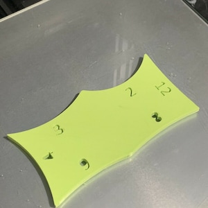 May include: A lime green plastic template with the numbers 2, 12, 3, and 9 printed on it.
