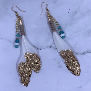 May include: A pair of gold glitter feather earrings with turquoise and white beads and a gold chain dangle.