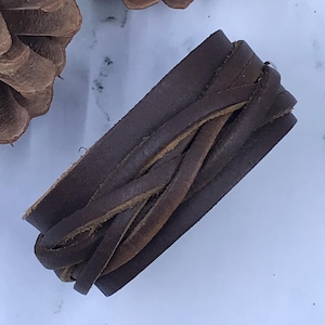 May include: A dark brown leather bracelet with a braided design. The bracelet is made of several strips of leather woven together. The bracelet is a wrap style and appears to be unworn.