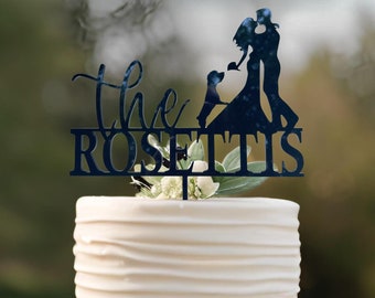 May include: A white wedding cake with a black silhouette cake topper featuring a couple kissing and a dog. The topper says "The Rosettis".