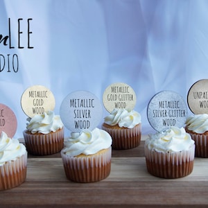 May include: Cupcakes with white frosting and wooden toppers labeled "Metallic Rose Gold Wood", "Metallic Gold Wood", "Metallic Silver Wood", "Metallic Gold Glitter Wood", "Metallic Silver Glitter Wood", and "Unpainted Wood". The image includes the "designLEE STUDIO" logo.