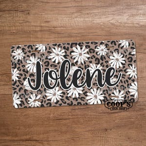 May include: A brown and black leopard print background with white daisies and the name "Jolene" in black cursive lettering. The bottom right corner has a white logo that says "Coop's Sign Shop".