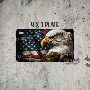 May include: A license plate featuring a detailed image of an American bald eagle with a yellow beak and piercing gaze, set against a backdrop of the American flag. The plate is labeled "4 X 7 PLATE" and includes the text "DO NOT COPY".