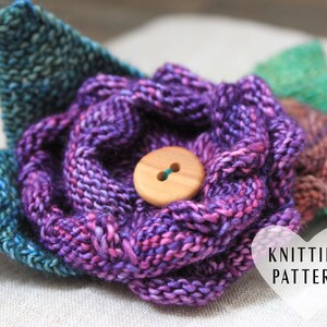 Może przedstawiać: Brozka w kształcie kwiatu wykonana na drutach w odcieniach fioletu, różu i błękitu. Kwiat ma drewniany guzik w środku. Tekst "Knitting Pattern" jest widoczny w prawym dolnym rogu obrazu.