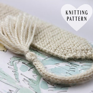 May include: A beige knitted bookmark with a tassel. The bookmark is lying on a page of a book with illustrations.