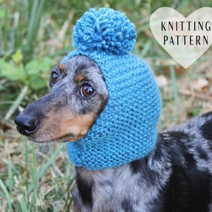 Peut inclure: Un teckel portant un bonnet bleu tricoté avec un pompon sur le dessus. Le bonnet a un rabat qui couvre les oreilles du chien. Le chien regarde vers la droite. L'image contient le texte "Knitting Pattern" dans un cœur blanc.