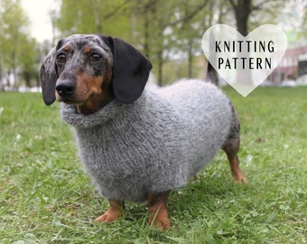 May include: A dachshund wearing a gray knitted sweater. The sweater has a turtleneck and is a loose fit. The dog is standing on green grass. The text "Knitting Pattern" is written in a white heart shape.