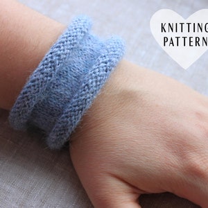 May include: A light blue knitted bracelet with a simple design. The bracelet is worn on a person's wrist.