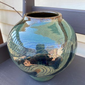 May include: A round, green ceramic vase with a dark brown rim and a swirling, abstract design in shades of blue and green.