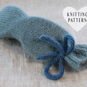 Peut inclure: Un masque pour les yeux en tricot bleu sarcelle avec un ruban bleu noué autour. Le masque pour les yeux est sur une surface en tissu brun clair. "Modèle de tricot" est écrit sur une étiquette en forme de cœur blanche.
