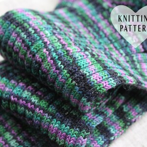 May include: A close-up of a folded knitted fabric in shades of green, purple, and black. The fabric has a striped pattern and is made with a fine yarn. The text "Knitting Pattern" is visible in a heart-shaped frame.