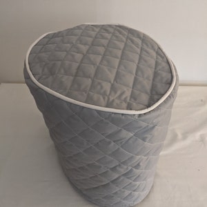May include: A light gray quilted appliance cover with a white trim. The cover has a diamond pattern and is designed to fit over a kitchen appliance. The cover is made of a soft, padded material.