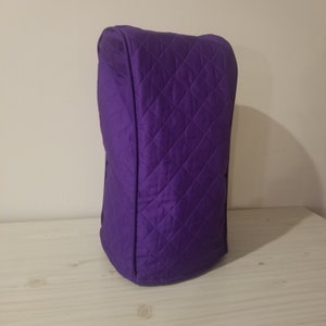 May include: A quilted, purple appliance cover. The cover is a solid, vibrant purple color and features a diamond pattern created by the stitching. The cover is designed to fit over a kitchen appliance, such as a blender or food processor.