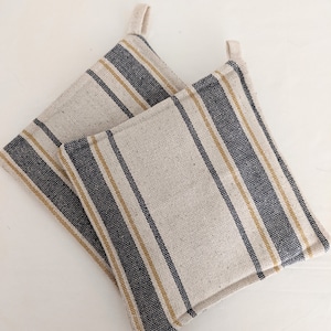 May include: Two striped pot holders with a cream background, black stripes, and gold stripes. The pot holders have a loop handle on each side.