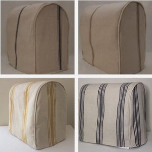 Könnte beinhalten: Beige Toaster-Abdeckungen mit vertikalen Streifenmustern. Die Abdeckungen haben abgerundete Oberteile und sind aus einem strukturierten Stoff gefertigt. Eine Abdeckung hat dunkelblaue Streifen, eine andere gelbe Streifen.