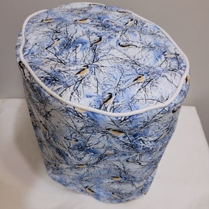 Può includere: Una copertura in tessuto blu e bianco con un motivo di uccelli invernali. La copertura ha un bordo bianco attorno al bordo superiore.