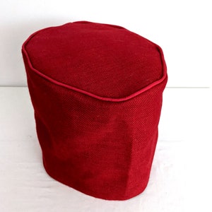 May include: A red fabric ottoman with a slightly rounded top and a dark red trim around the top edge.