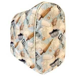 May include: A blue and white patterned kitchen appliance cover with a design of rolling pins, whisks, and other baking tools. The cover has a white trim around the edges.