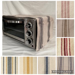 Puede incluir: Un horno tostador plateado con una cubierta de tela a rayas beige y negra. La cubierta tiene un bolsillo en el lateral. La tela está disponible en una variedad de colores y patrones.