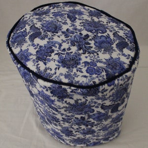 May include: A white and blue floral patterned fabric cover for a kitchen appliance. The cover has a dark blue trim around the top edge.