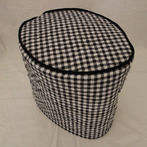 May include: Black and white checkered quilted fabric cover for a kitchen appliance. The cover has a black trim around the top edge.