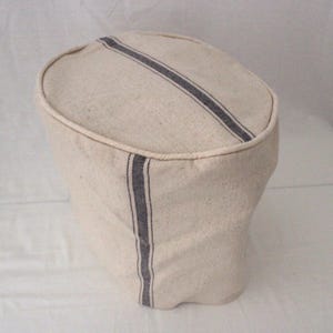 May include: A beige fabric hat with a dark blue stripe running diagonally across the top and a vertical stripe down the side. The hat has a rounded top and a curved brim.