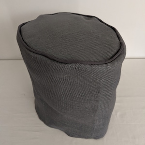 May include: A gray fabric ottoman with a rounded top and a dark gray trim around the top edge.