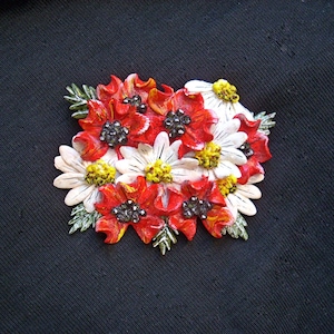 May include: A bouquet of red and white flowers with black centres. The flowers are made of polymer clay and are arranged in a cluster. The flowers are on a black background.