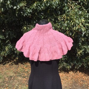 Op de afbeelding: Een roze gebreide cowl met een gerimpelde rand. De cowl wordt gedragen door een mannequin met een zwarte jurk.