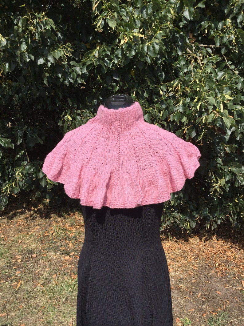 Op de afbeelding: Een roze gebreide cowl met een gerimpelde rand. De cowl wordt gedragen door een mannequin met een zwarte jurk.