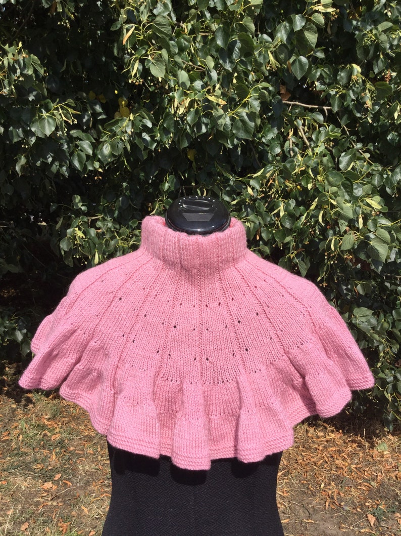 Op de afbeelding: Een roze gebreide cowl met een gerimpelde rand. De cowl is gemaakt van een zacht, lichtgewicht garen en heeft een delicaat opengewerkt patroon.