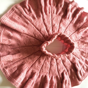 Op de afbeelding: Een stoffige roze gebreide rok met een gegolfde zoom. De rok is gemaakt met een delicaat steekpatroon en heeft een geplooide tailleband.
