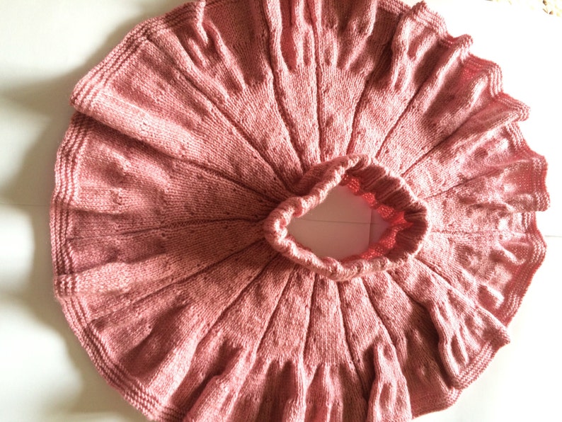 Op de afbeelding: Een stoffige roze gebreide rok met een gegolfde zoom. De rok is gemaakt met een delicaat steekpatroon en heeft een geplooide tailleband.