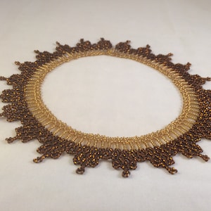 May include: A brown and gold beaded necklace with a scalloped edge. The necklace is made of small, round beads that are arranged in a pattern. The necklace is a statement piece that would add a touch of elegance to any outfit.
