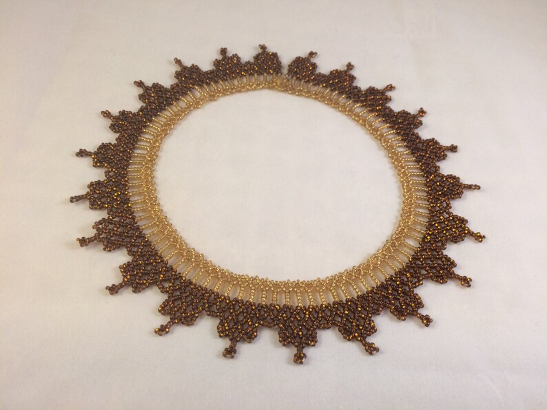 May include: A brown and gold beaded necklace with a scalloped edge. The necklace is made of small, round beads that are arranged in a pattern.