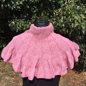 Op de afbeelding: Een roze gebreide cowl met een gerimpelde rand. De cowl is gemaakt van een zacht, delicaat garen en heeft een hoge hals.
