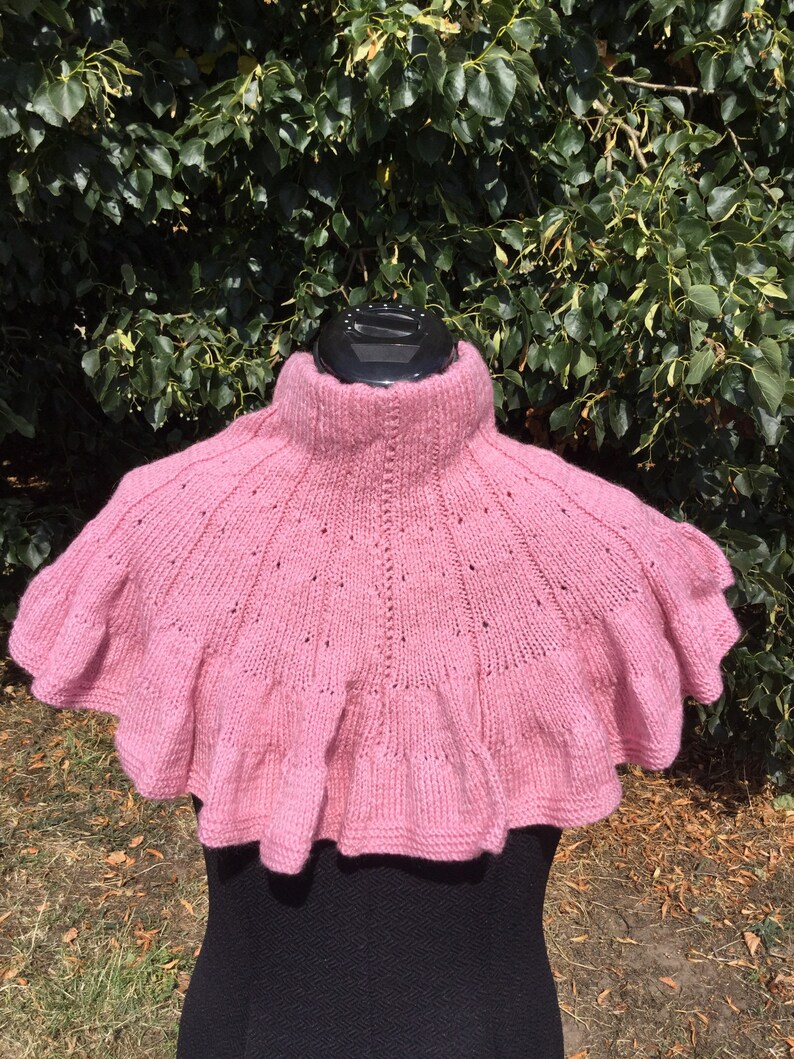 Op de afbeelding: Een roze gebreide cowl met een gerimpelde rand. De cowl is gemaakt van een zacht, delicaat garen en heeft een hoge hals.