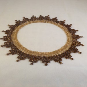 May include: A brown and gold beaded necklace with a scalloped edge. The necklace is made of small, round beads that are arranged in a circular pattern.