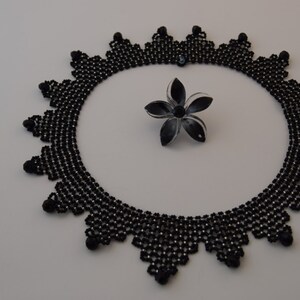 May include: A black beaded necklace with a delicate, intricate design. The necklace is circular and has a scalloped edge.