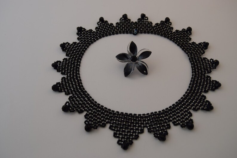 May include: A black beaded necklace with a delicate, intricate design. The necklace is circular and has a scalloped edge.