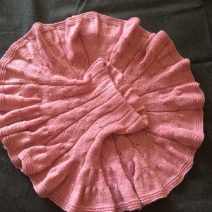 Op de afbeelding: Een roze gebreid babydekentje met een gegolfde rand.