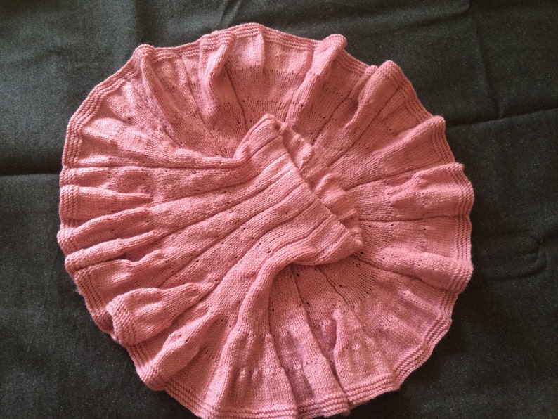 Op de afbeelding: Een roze gebreid babydekentje met een gegolfde rand.