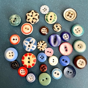 May include: A selection of assorted buttons in various colours and designs. The buttons are circular, with two or four holes, and feature a range of colours including red, blue, green, and brown. Some have patterns.
